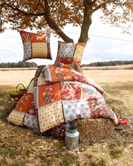 Werbefotografie, Outdooraufnahme, bunte, gestapelte Decken und Kissen unter einem Baum auf einer Wiese.
