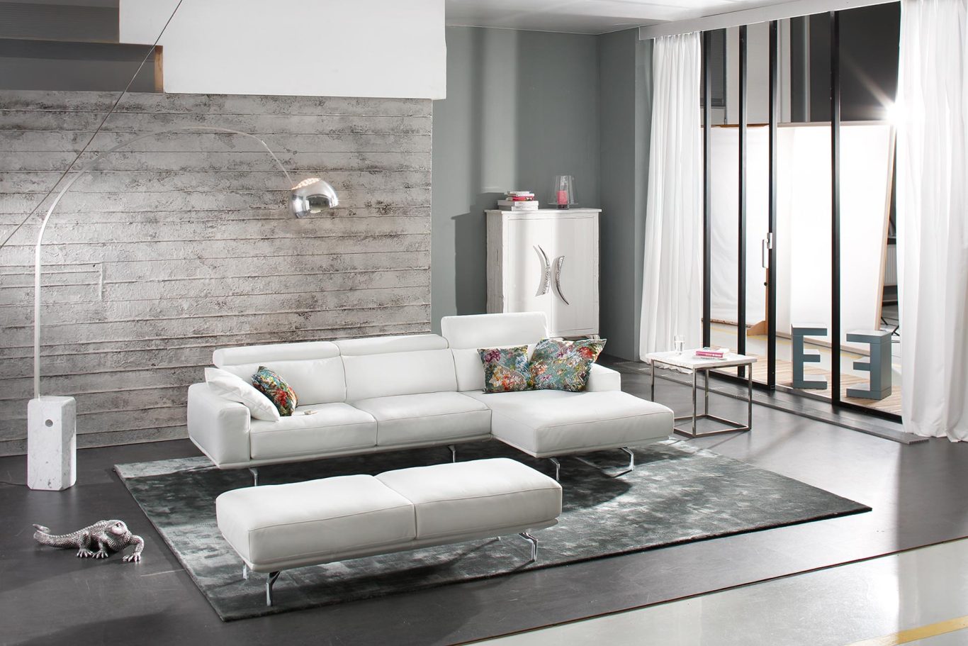 Helle, moderne Wohnlandschaft mit weißem Sofa, Teppich und großen Fenstern, unbearbeitete Aufnahme